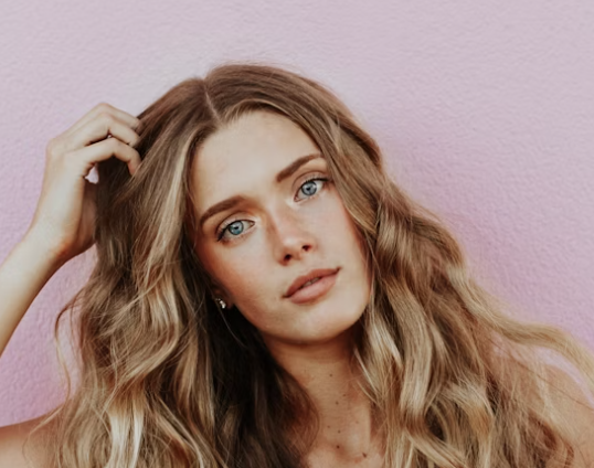 Woman with long wavy hair posing against a pink wall